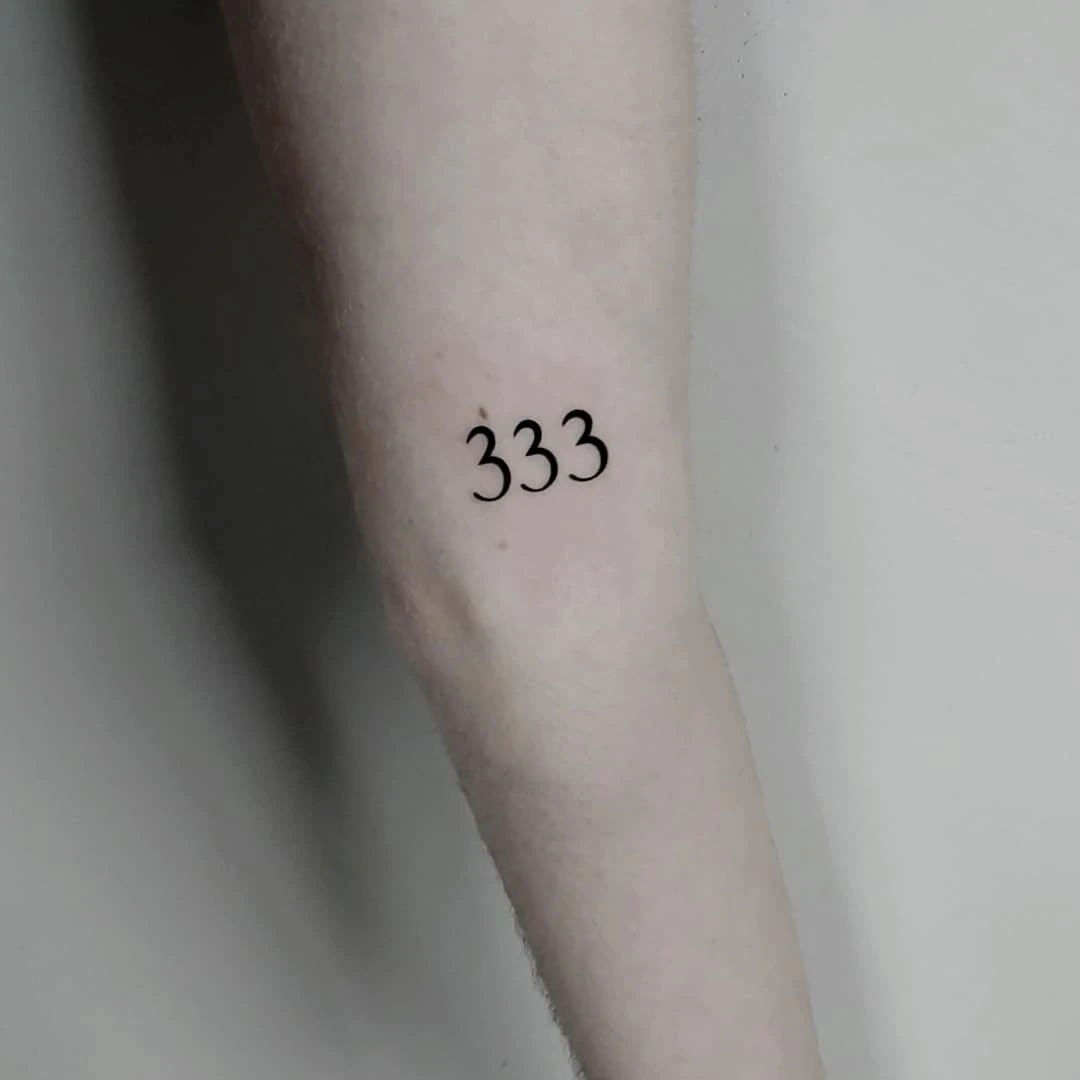 Image of a forearm displaying the number 333 tattooed on the skin