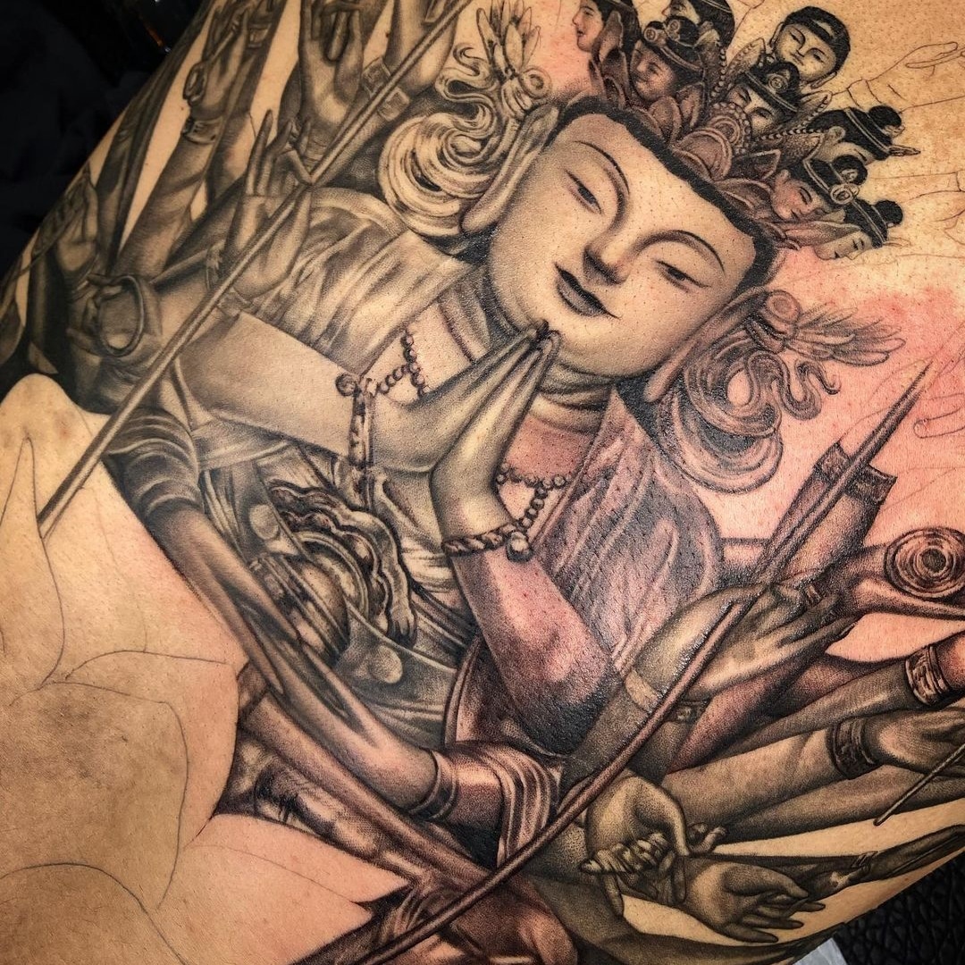 Detailed tattoo artwork of a Buddhist figure with multiple arms and expressions.