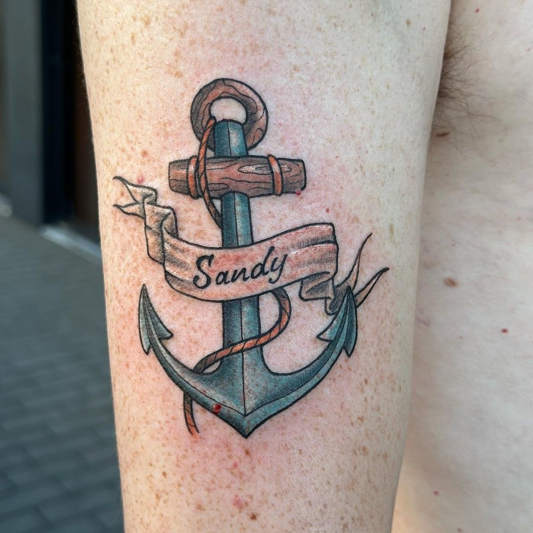 Tattoo of an anchor with the name Sandy on an arm