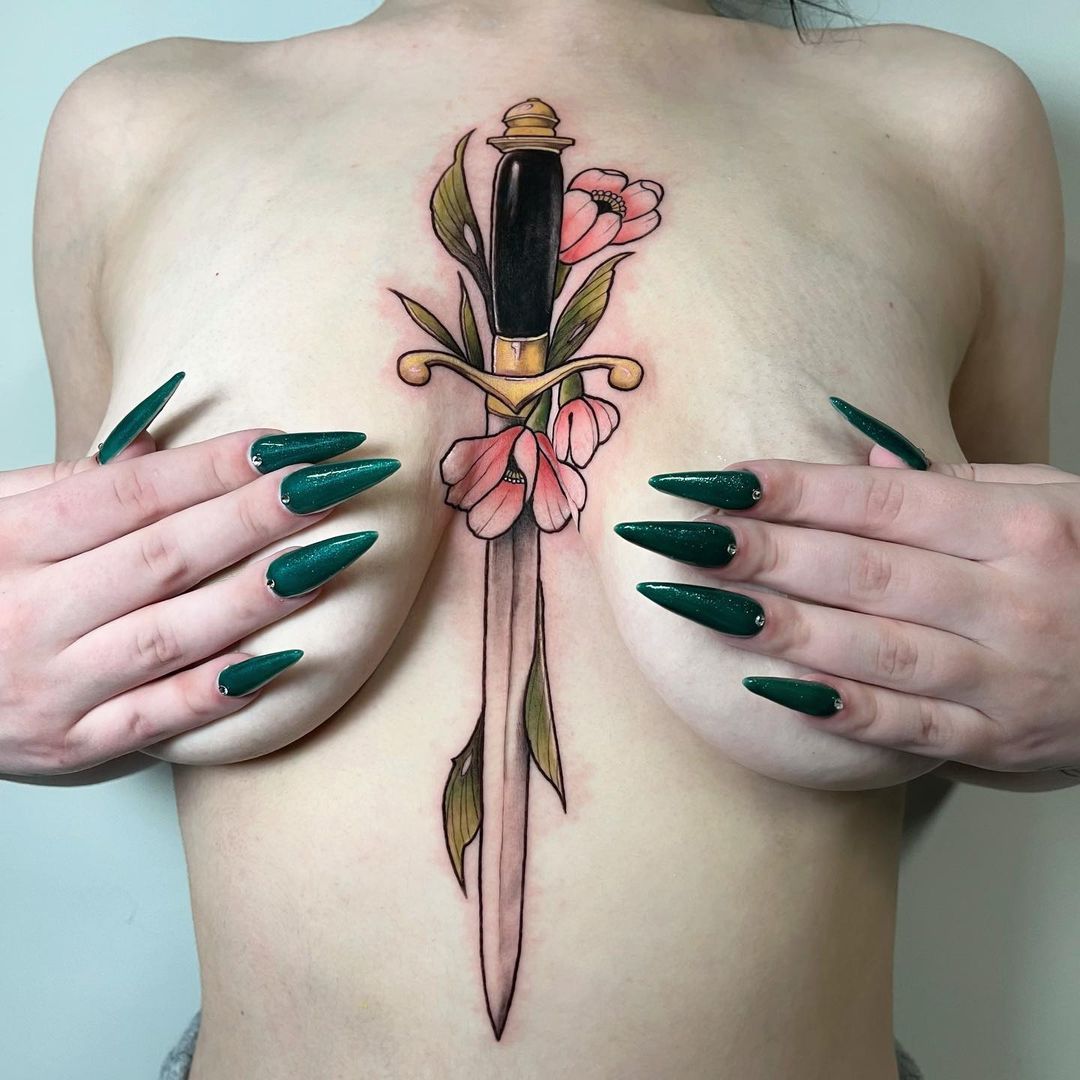 A striking tattoo of a dagger surrounded by flowers on a bare chest, featuring long green nails.