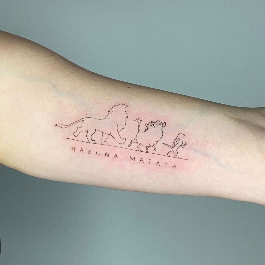 Tattoo featuring silhouette of lion, warthog, and meerkat with 'Hakuna Matata' text
