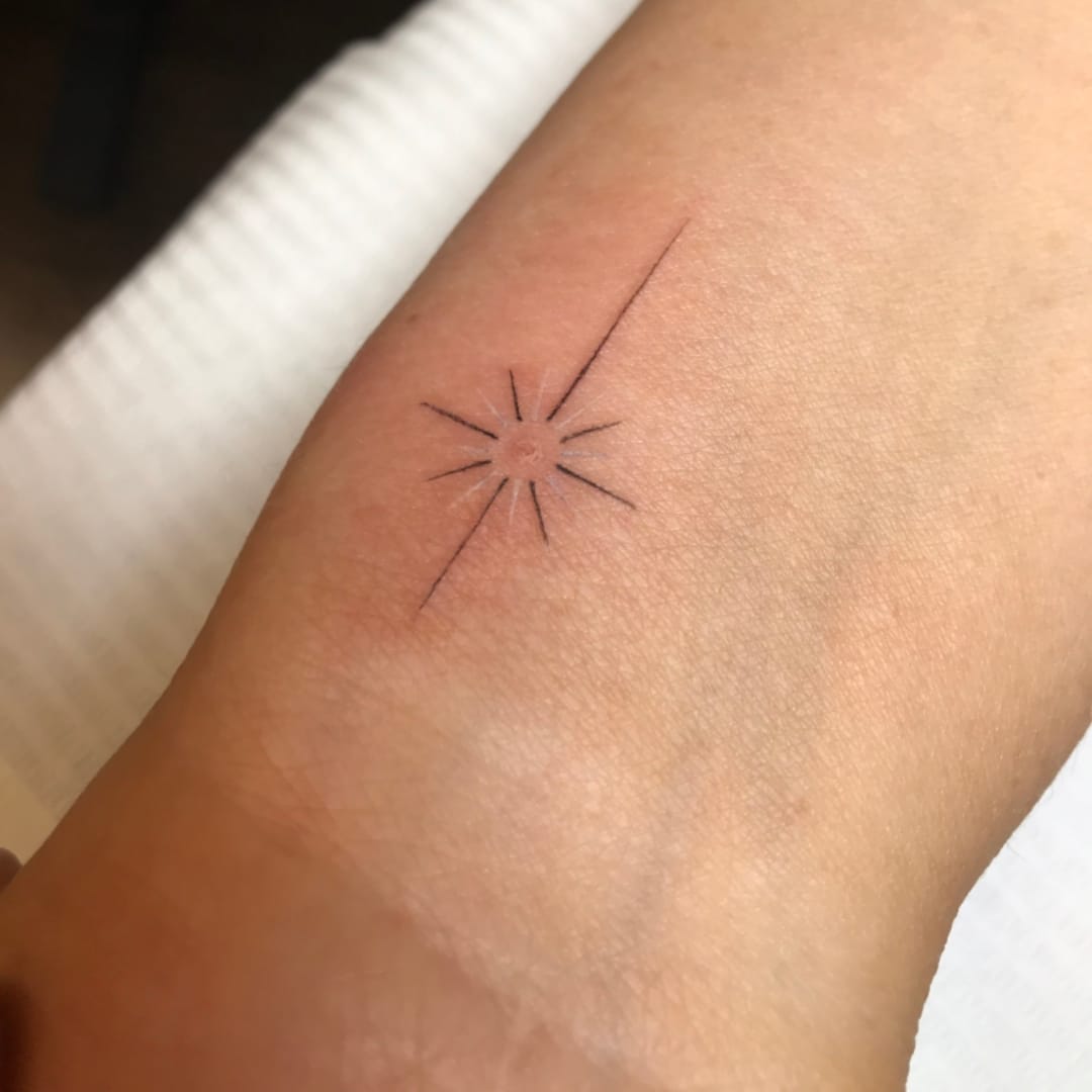 Minimalist tattoo resembling a sun on a wrist.